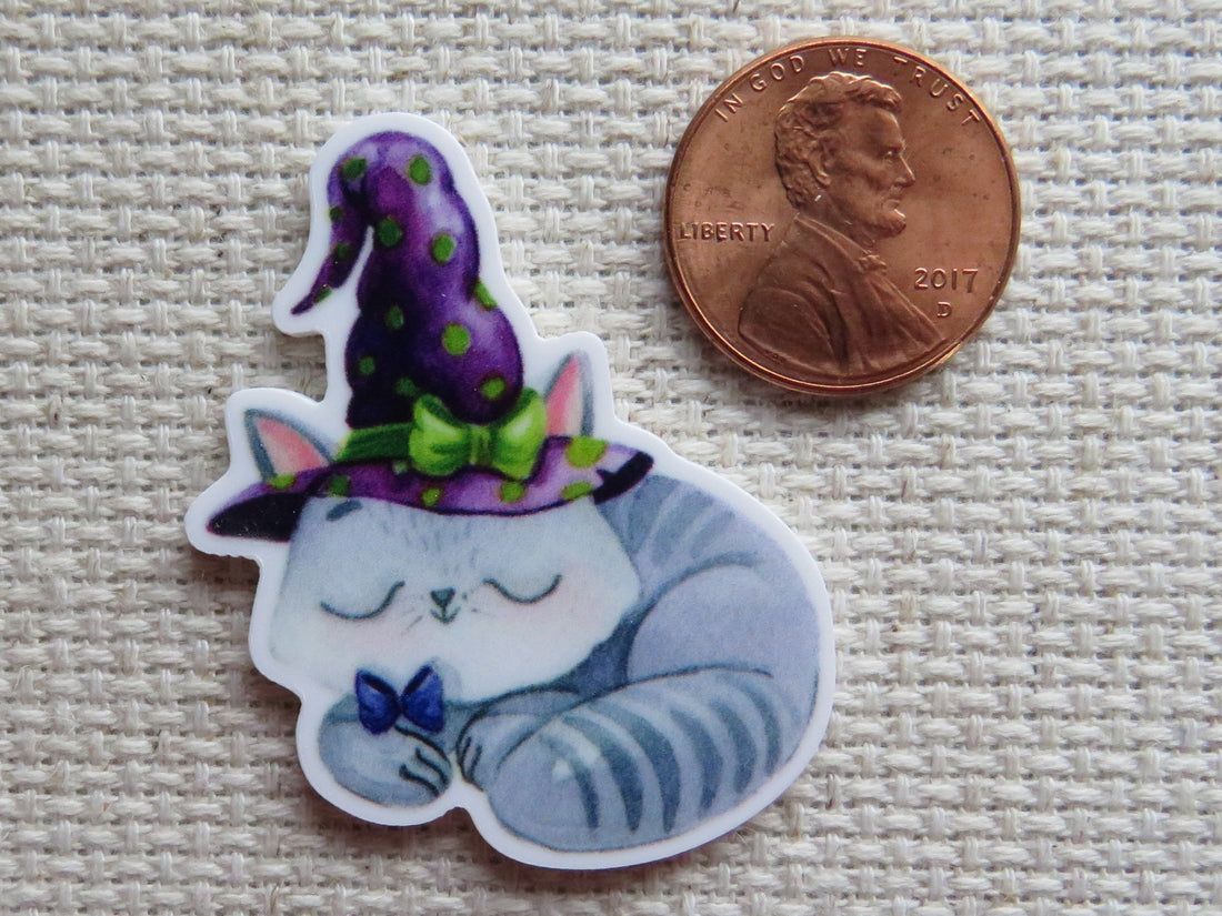 First view of stripped gray kitten is curled up asleep while wearing a purple witch's hat and a cute purple bow minder.